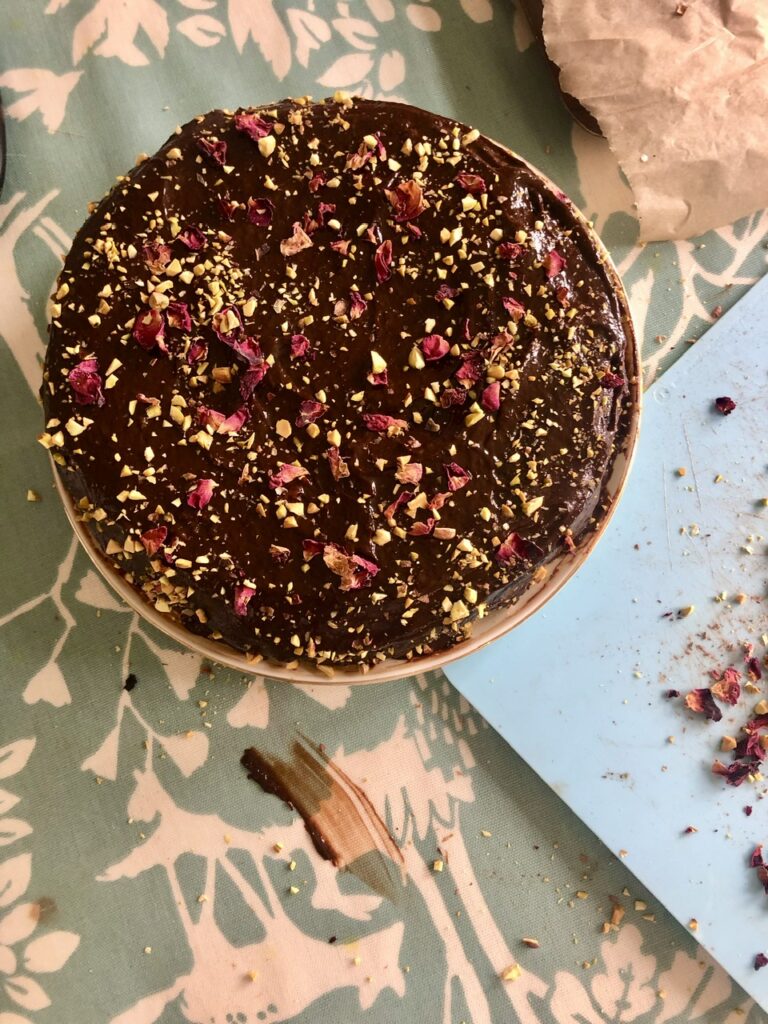 A decadent vegan chocolate cake topped with rose and pistachio